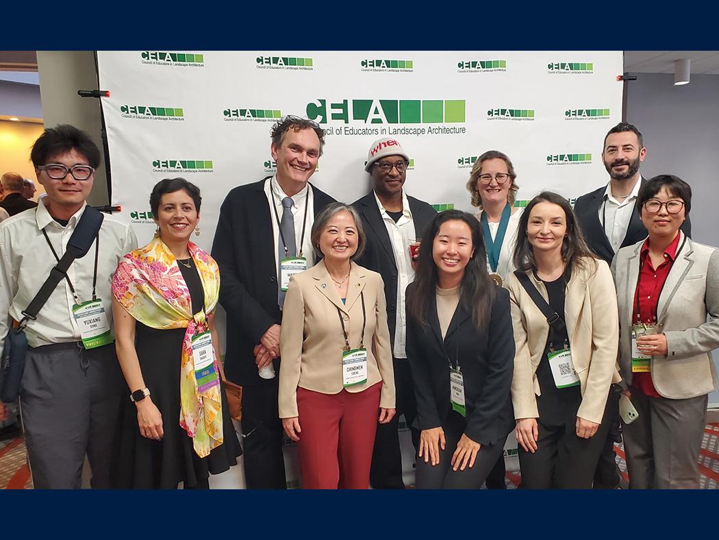 A group of people gathered in front of a green and white backdrop that reads "CELA."