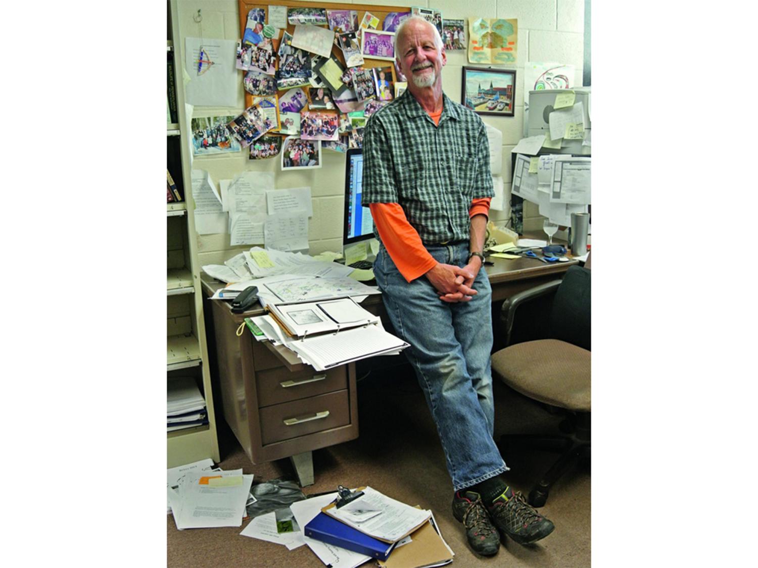 Chris Uhl in his office, leaning on his desk surrounded by papers, books and photos tacked to the wall.