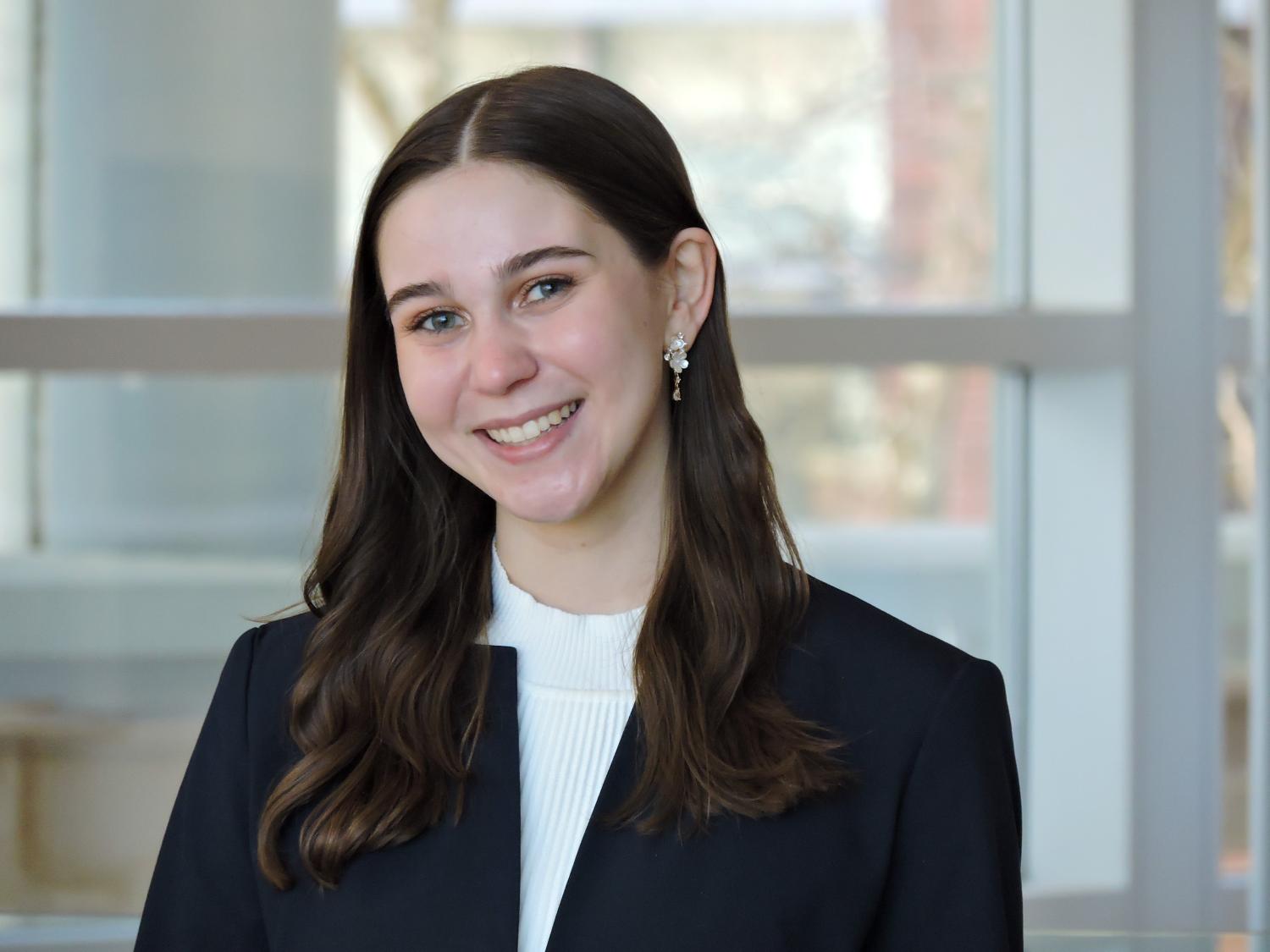 Emily Danczyk wears a black jacket and white blouse standing inside a modern building.