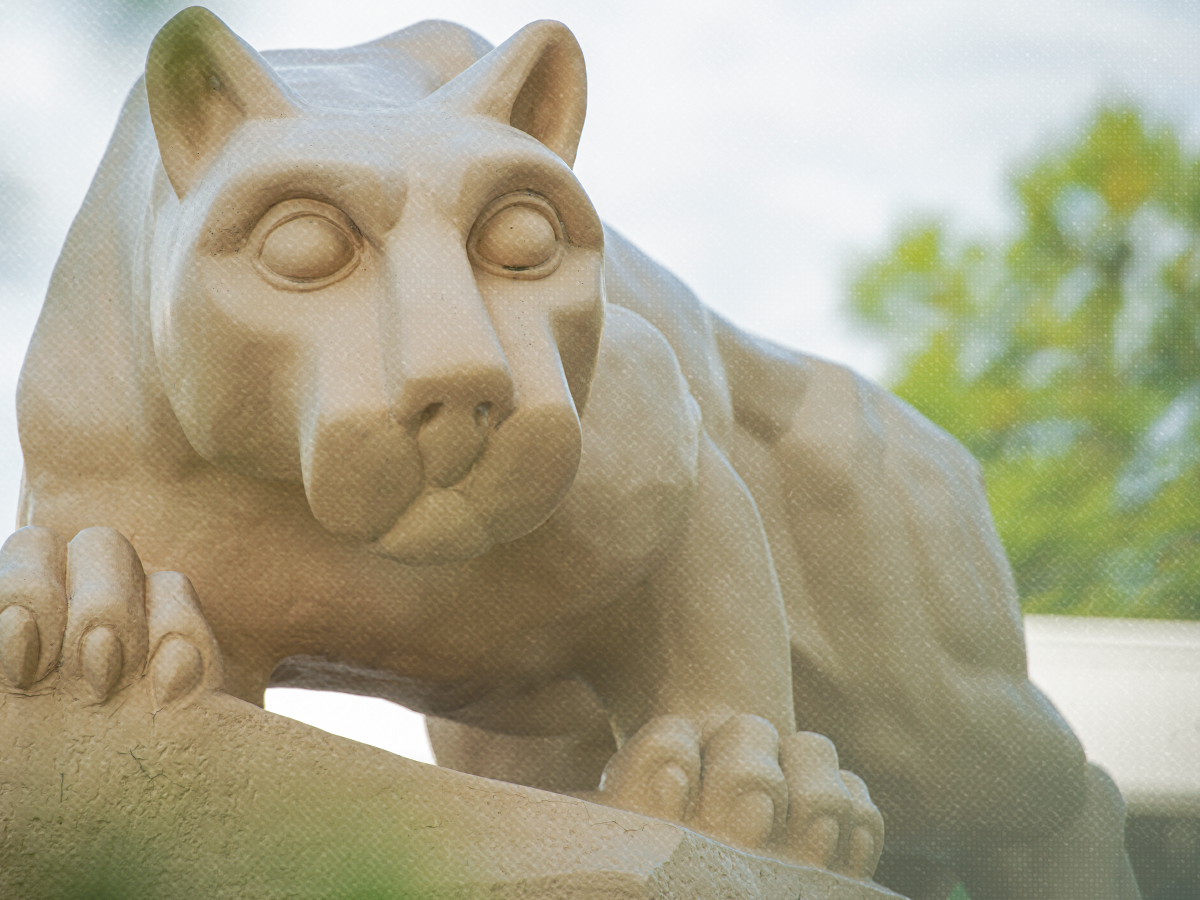 Close-up of the Penn State Fayette Lion Shrine, with the stone lion’s face and front paws visible against a softly blurred outdoor background.