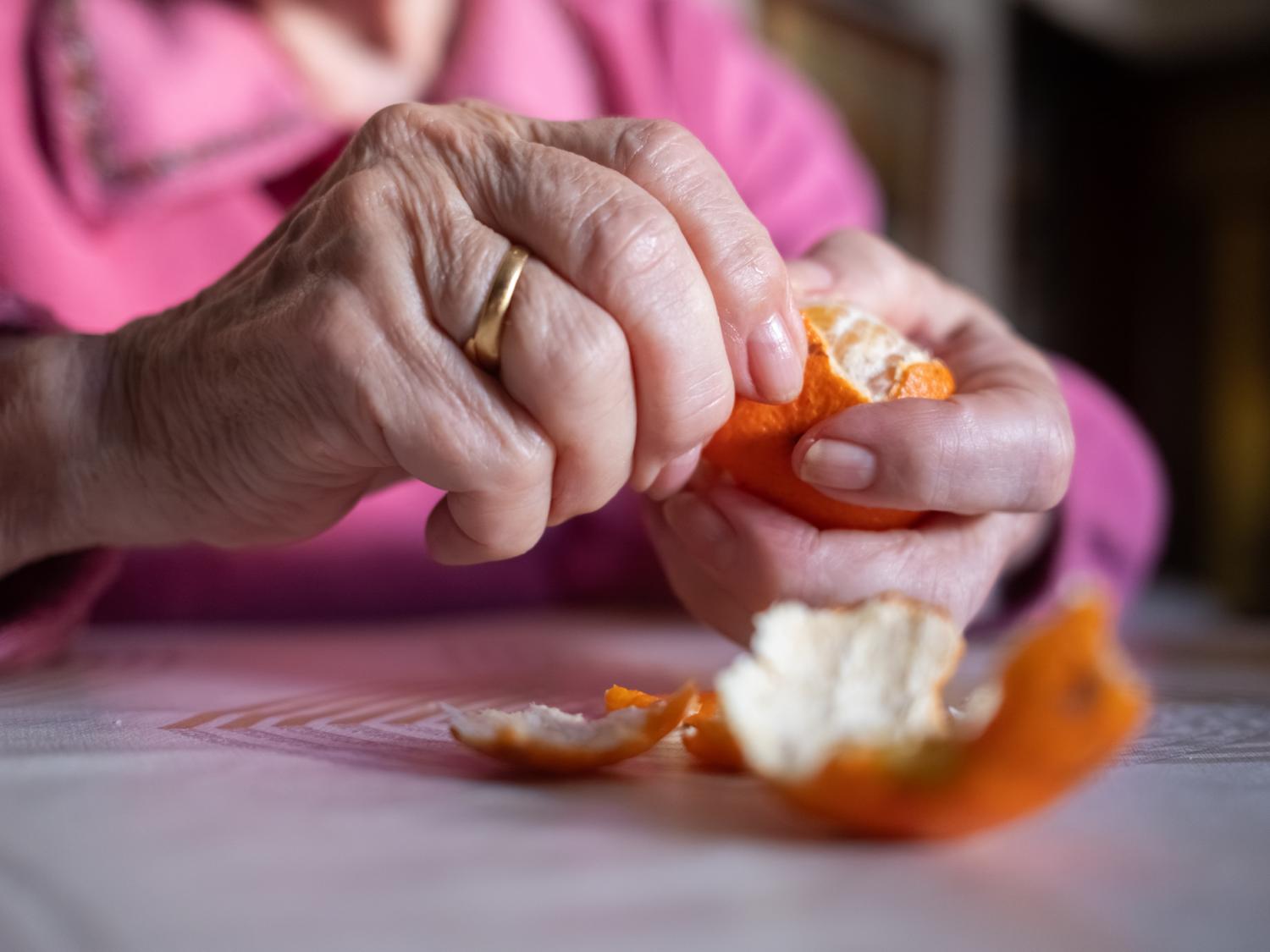 hands of an older woman peeling an orange