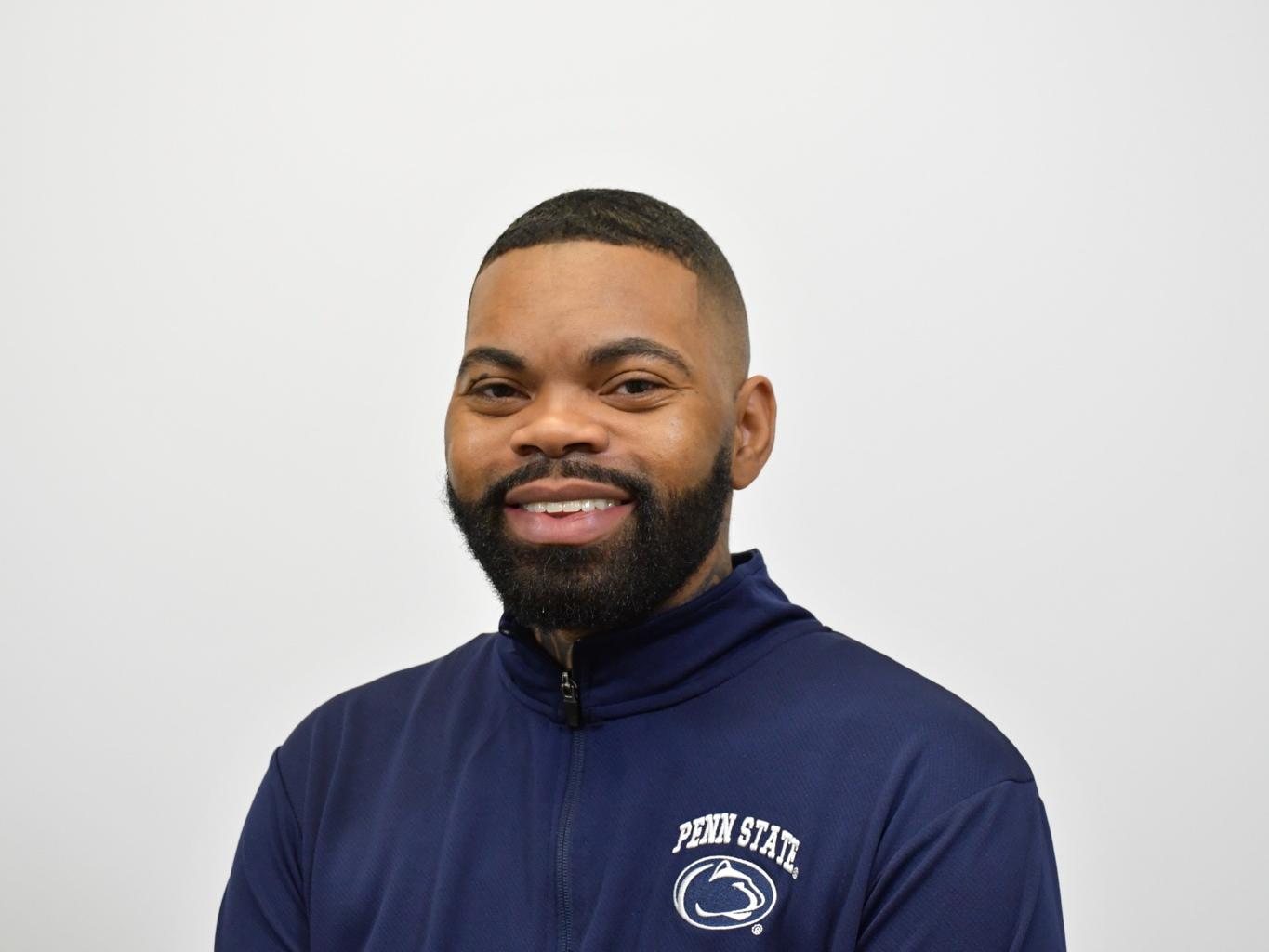 ML Brown, a Penn State College of Education doctoral candidate in special education, smiles in a headshot wearing a navy Penn State quarter-zip against a neutral background.