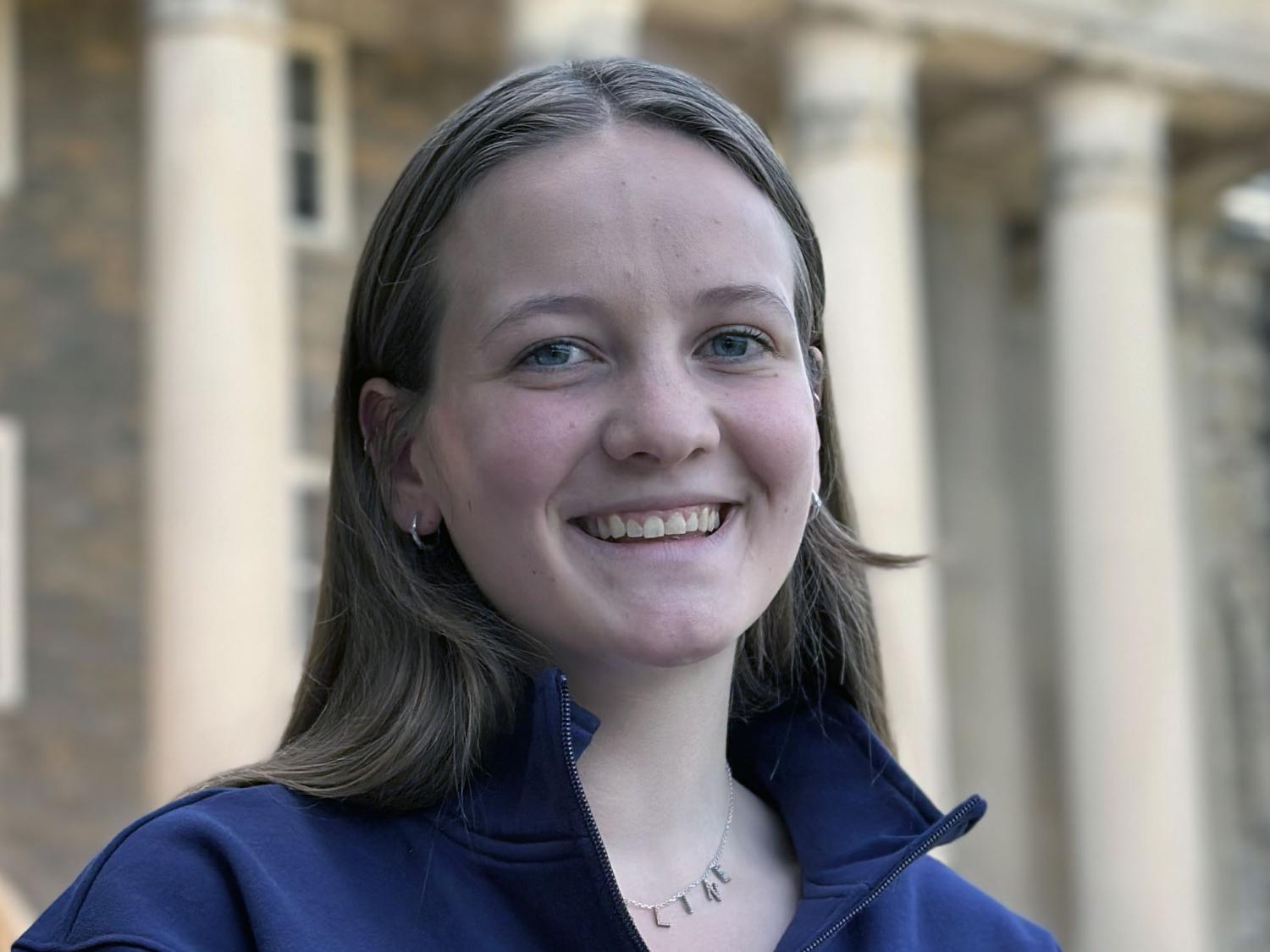 Maddie Shanafelt, a Penn State College of Education student, smiles in a headshot wearing a navy jacket in front of campus columns.