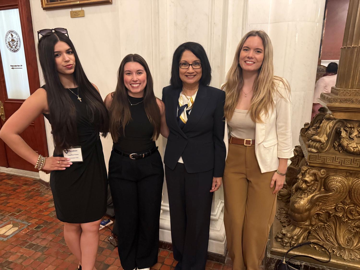 Four women pose together in a formal government building, dressed in professional attire.