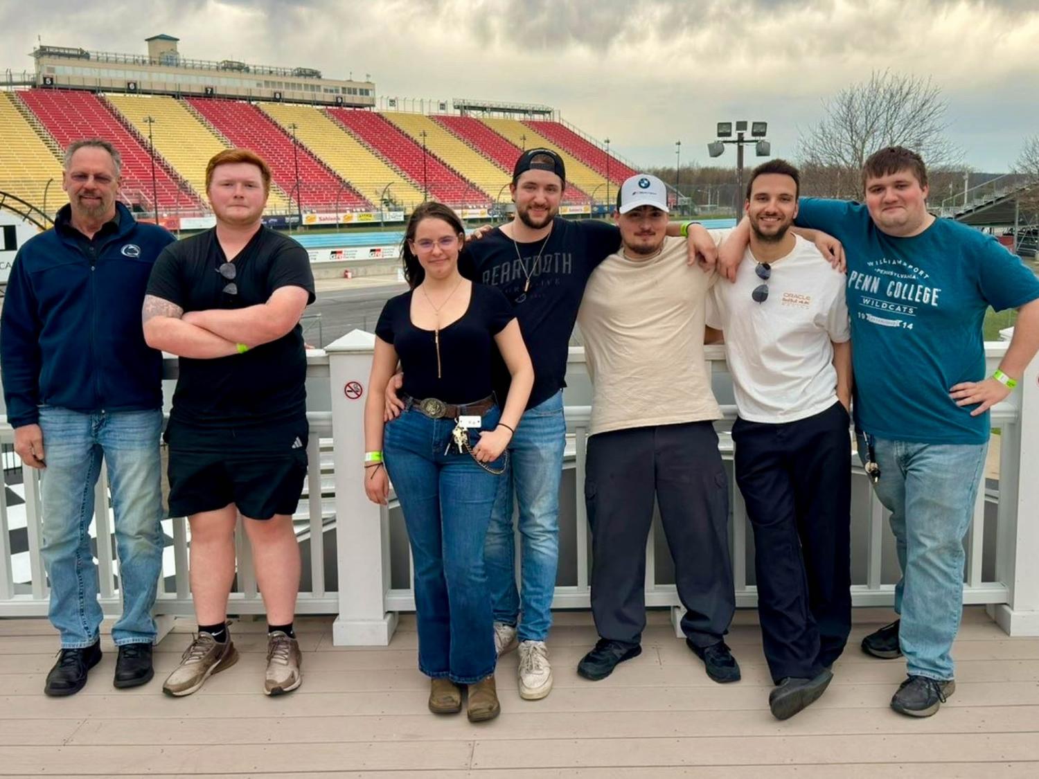 Seven people stand in a row at Watkins Glen International race track.
