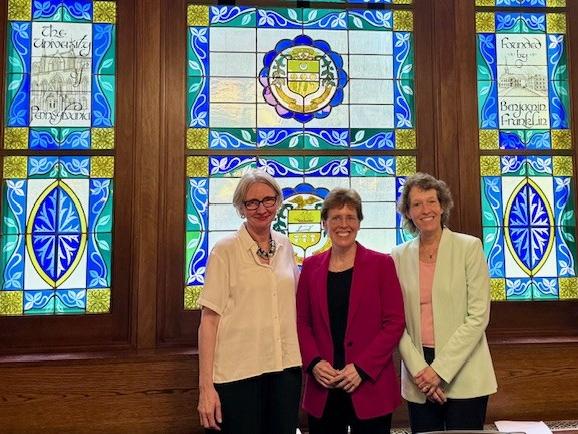 Three people stand in front of stained glass windows smiling. 
