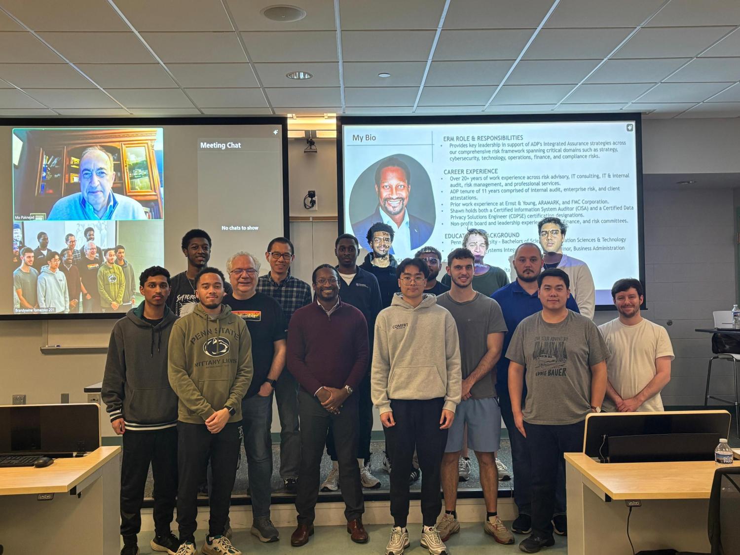 students, Shawn Manderson and professor positioned in front of projector with a Zoom call and presentation on it