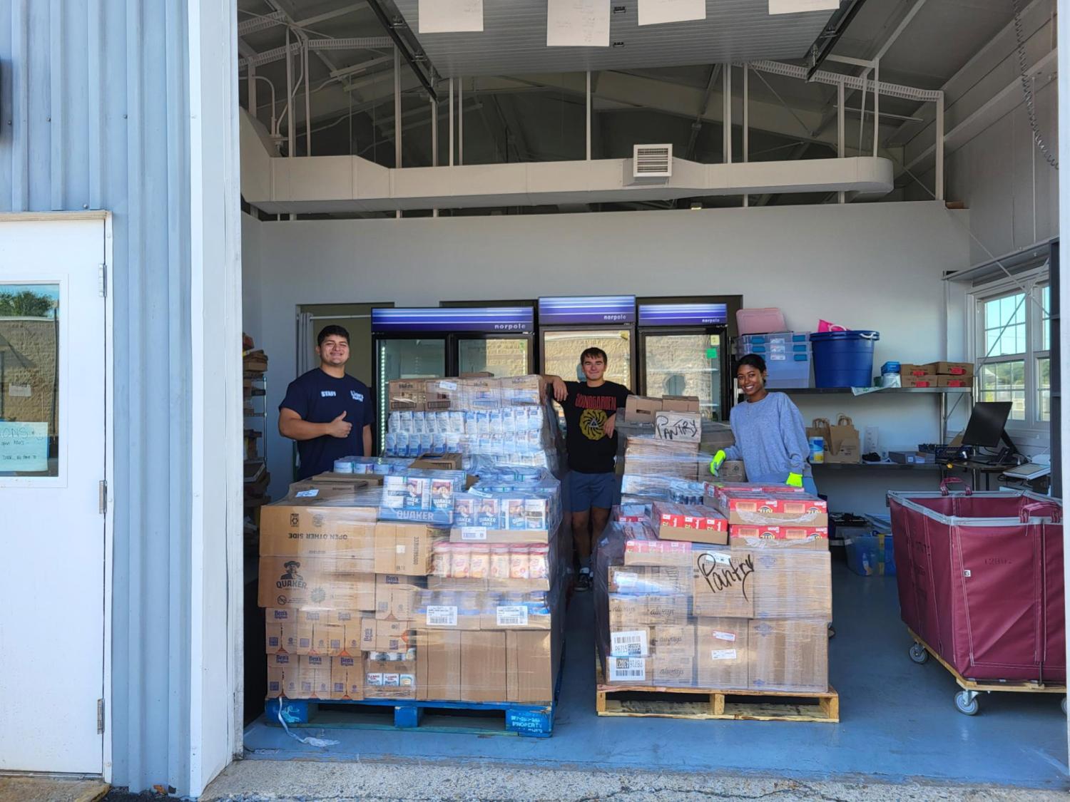 Three student volunteers pose with pallets of food at the Lions Pantry