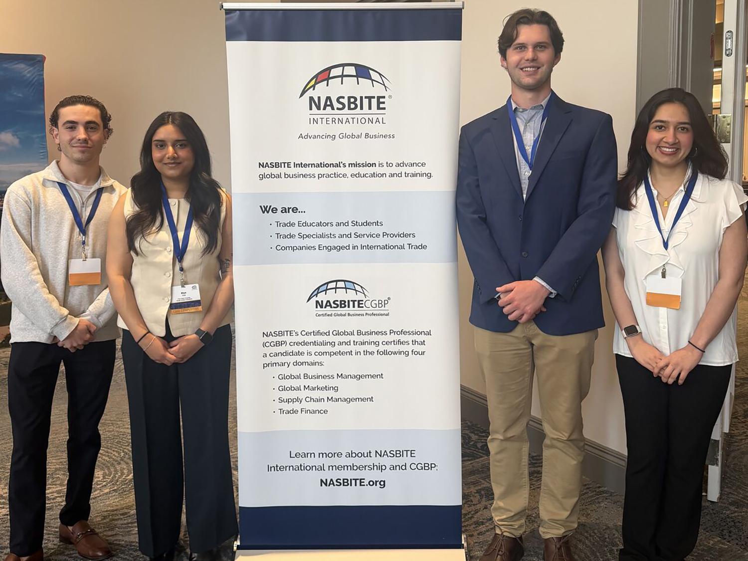 Two male and two female students stand on either side of a standup banner.