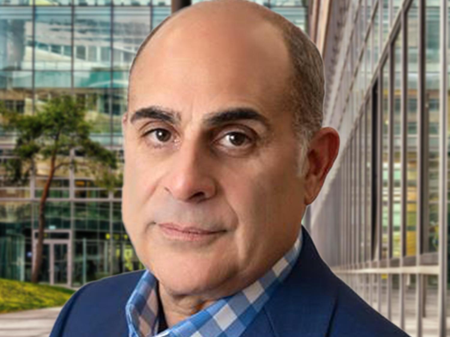 A head and shoulders photo of Ron Christy, who is wearing a blue sport jacket and a blue and white checked shirt.