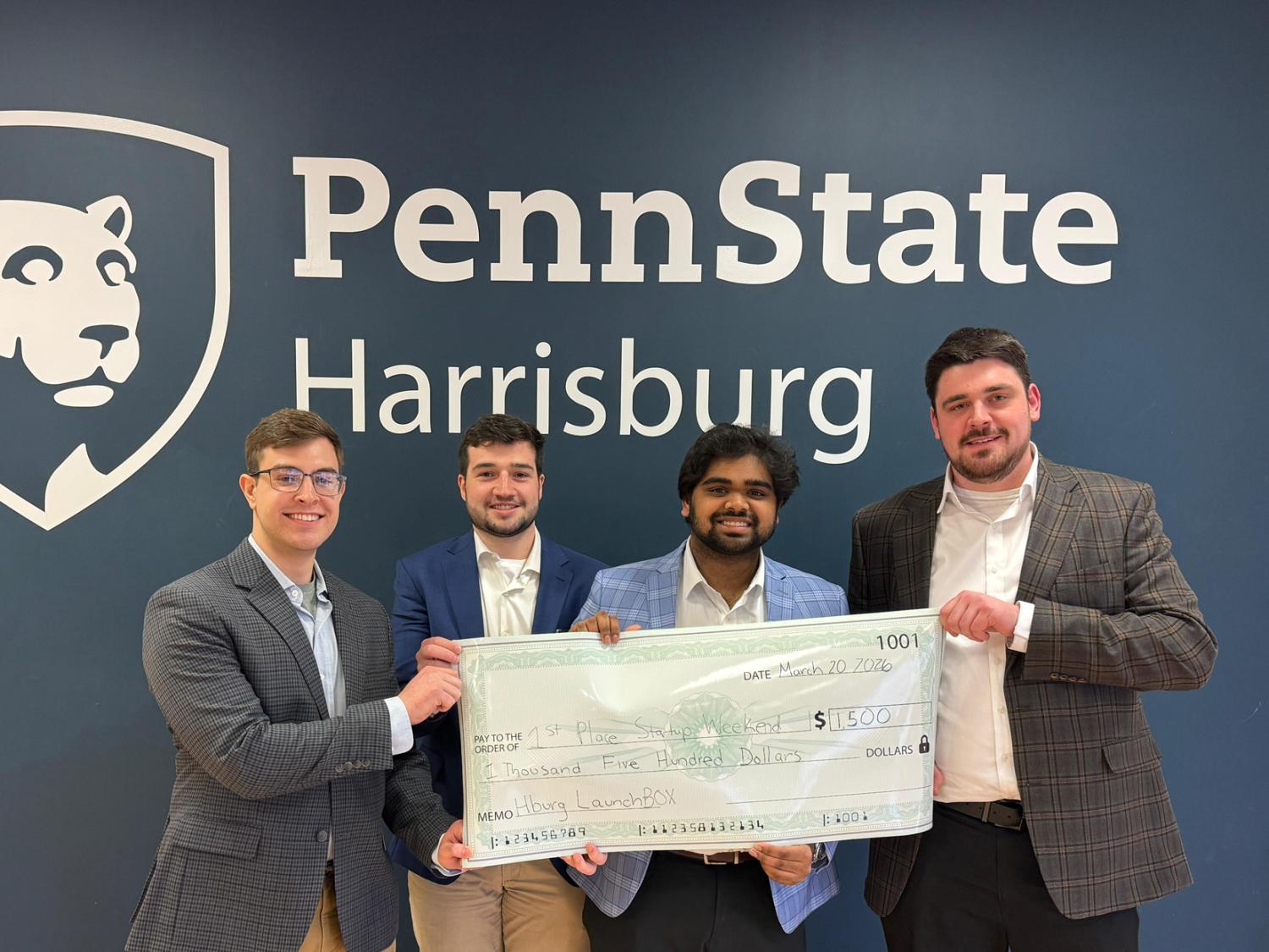 Four students hold up a large check in front of a Penn State Harrisburg sign