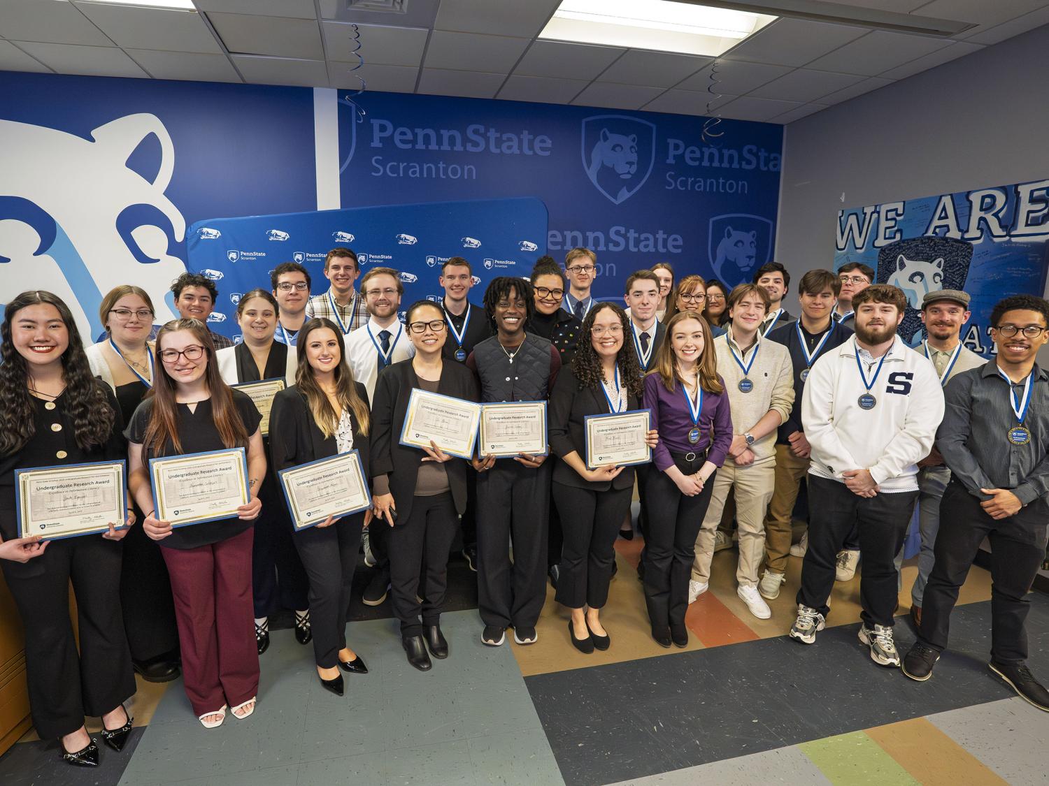 Student winners pose for a group photo holding their award certificates and ribbons