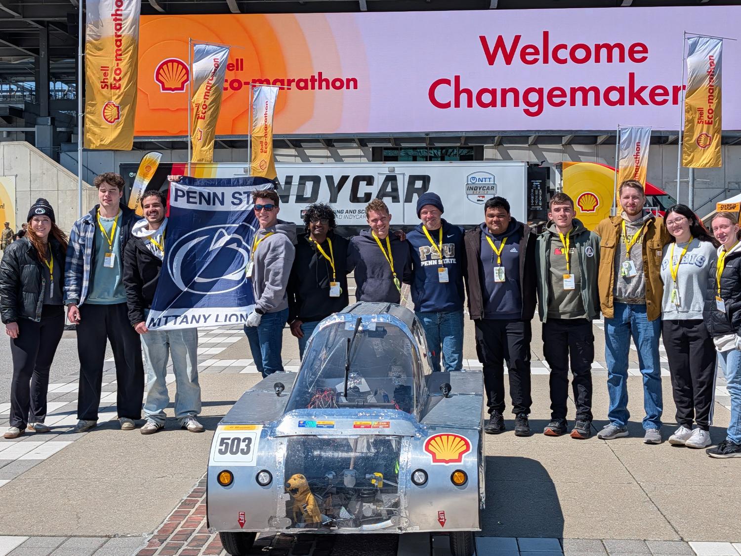 A photo of twelve members of the Eco-Marathon team standing in a row, behind their competition car, at the Indianapolis Motor Speedway.
