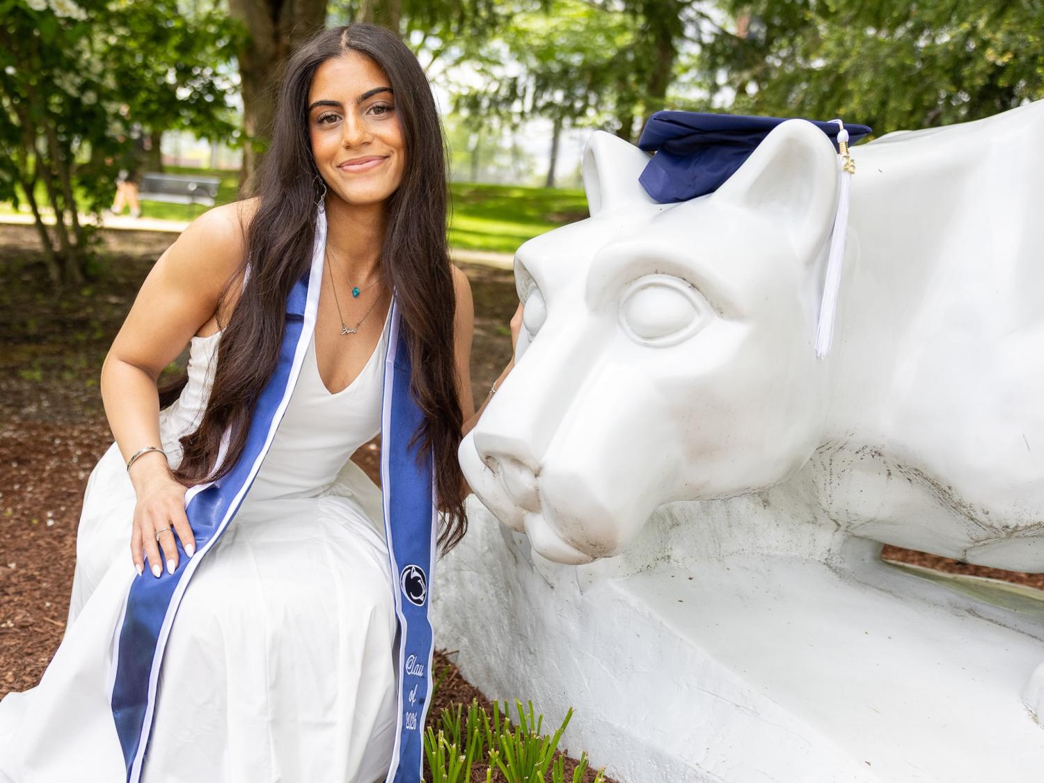 Amira squatting next to the lion shrine with a graduation cap on its head. 