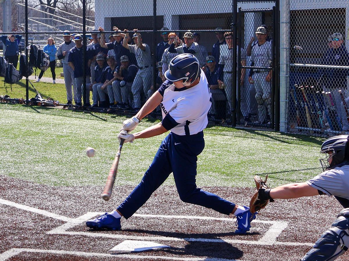 Jonathan Rauch swings at a pitch during a Penn State Altoona baseball game as teammates watch from the dugout