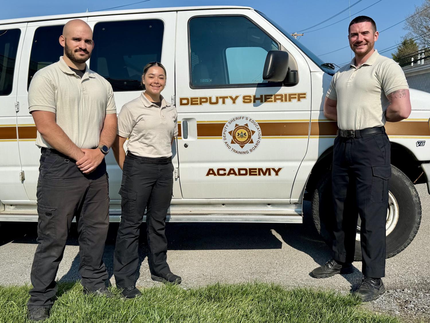 Three people stand against a Deputy Sheriff Academy van