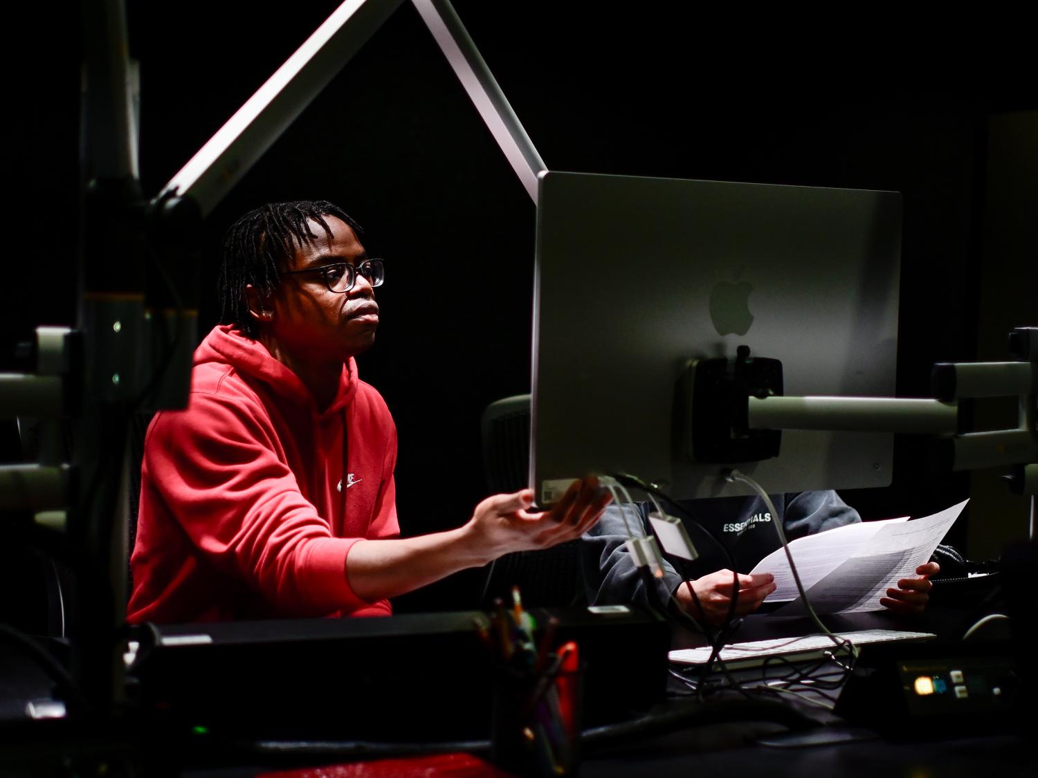 A student in a red sweatshirt a computer monitor.