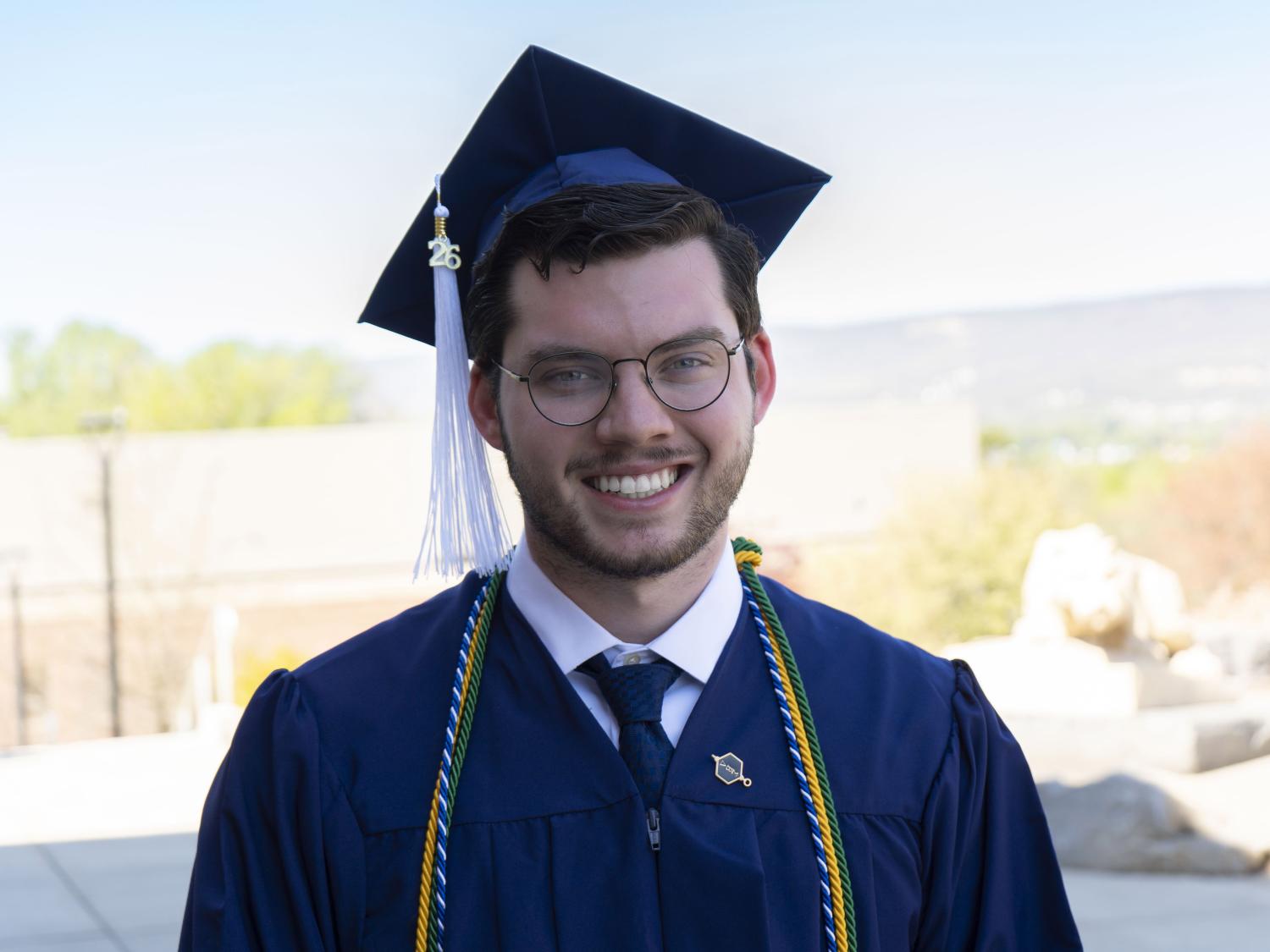 Penn State male graduate smiles for a photo wearing blue commencement reglia. 