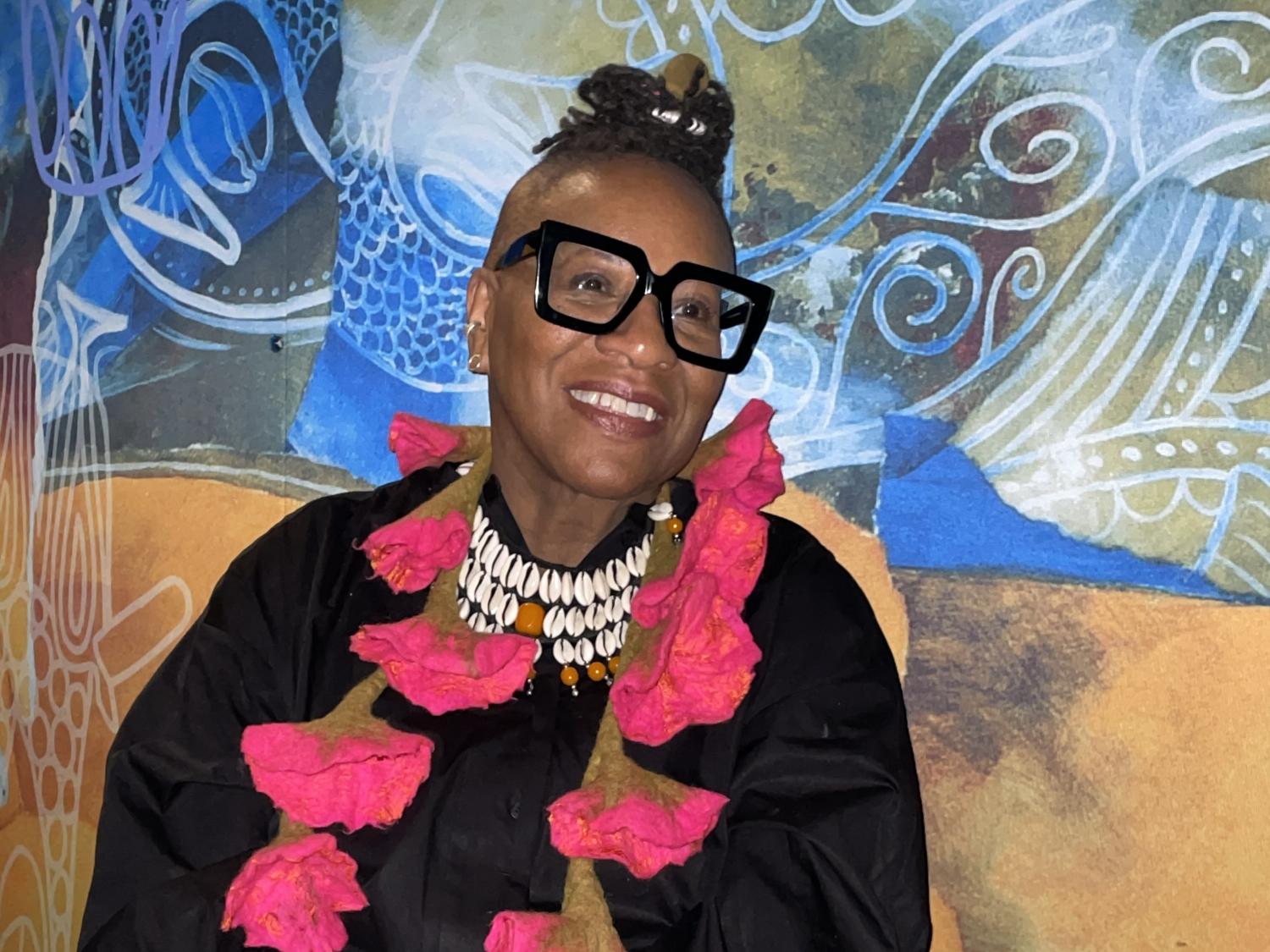Black woman with hair on top of her head, black glasses and bright pink necklace
