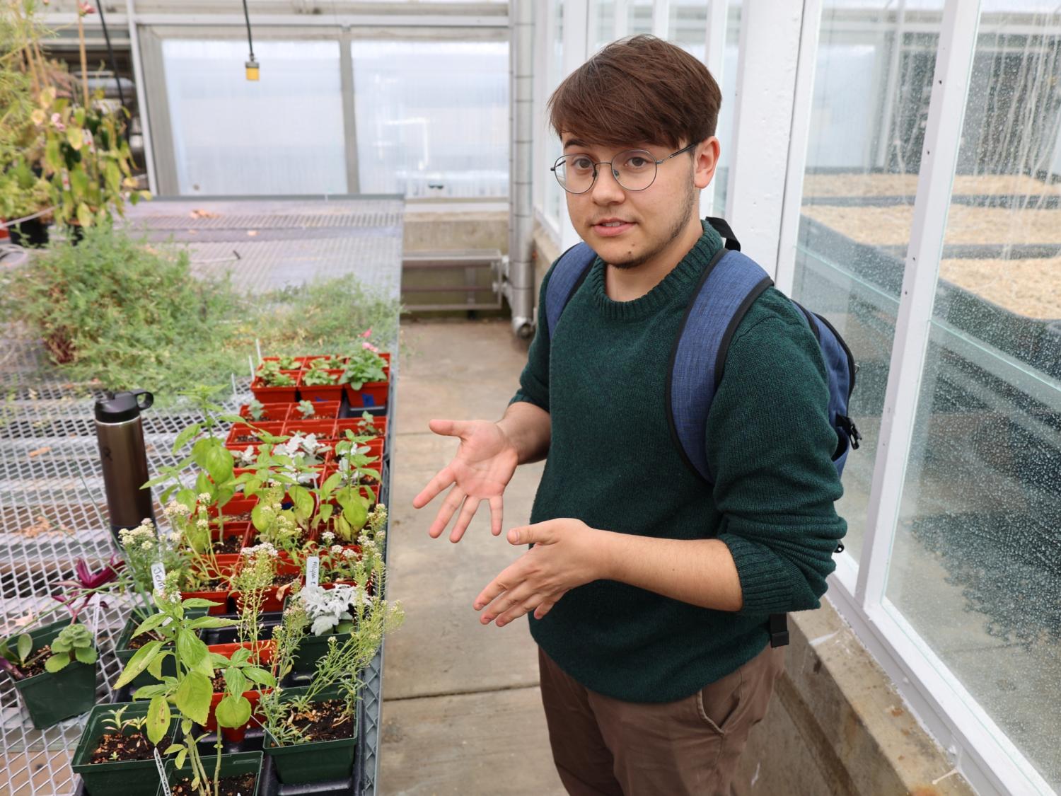 Grayson Lauer talking and gesturing to plants on a grow table inside a headhouse