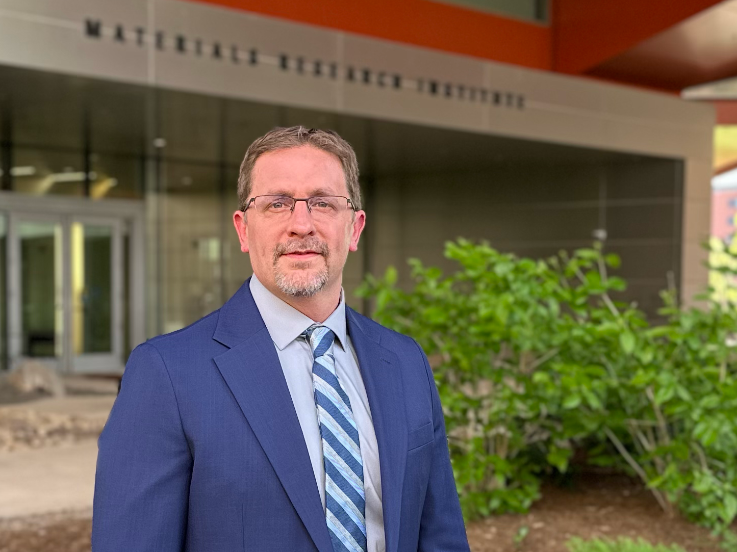 Person in a jacket and tie standing in front of the Materials Research Institute at University Park.