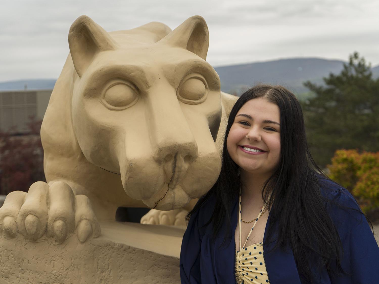 Penn State female graduate smiles for a photo wearing blue commencement reglia. 