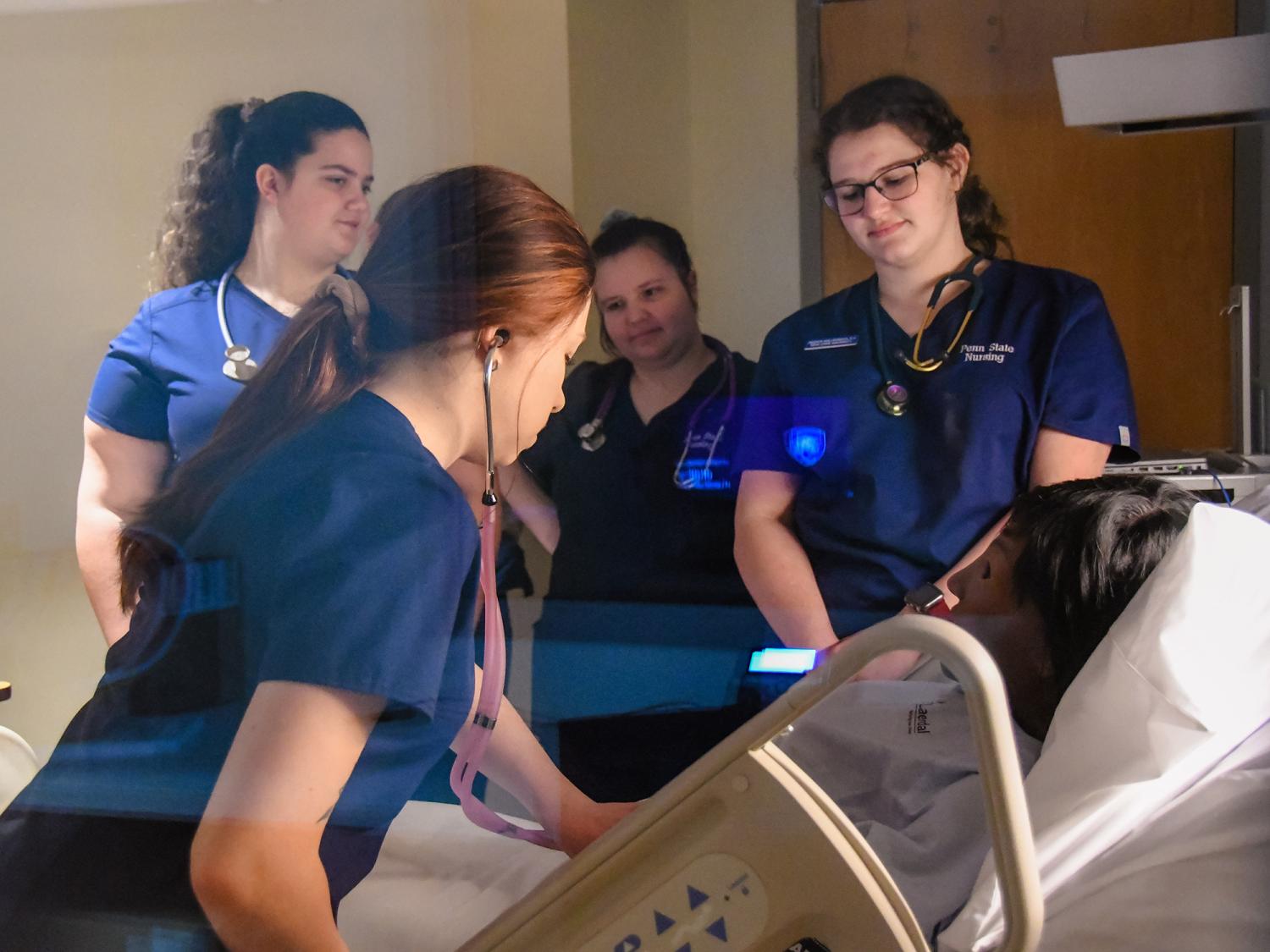 Four nursing students in blue uniforms attend a training manikin