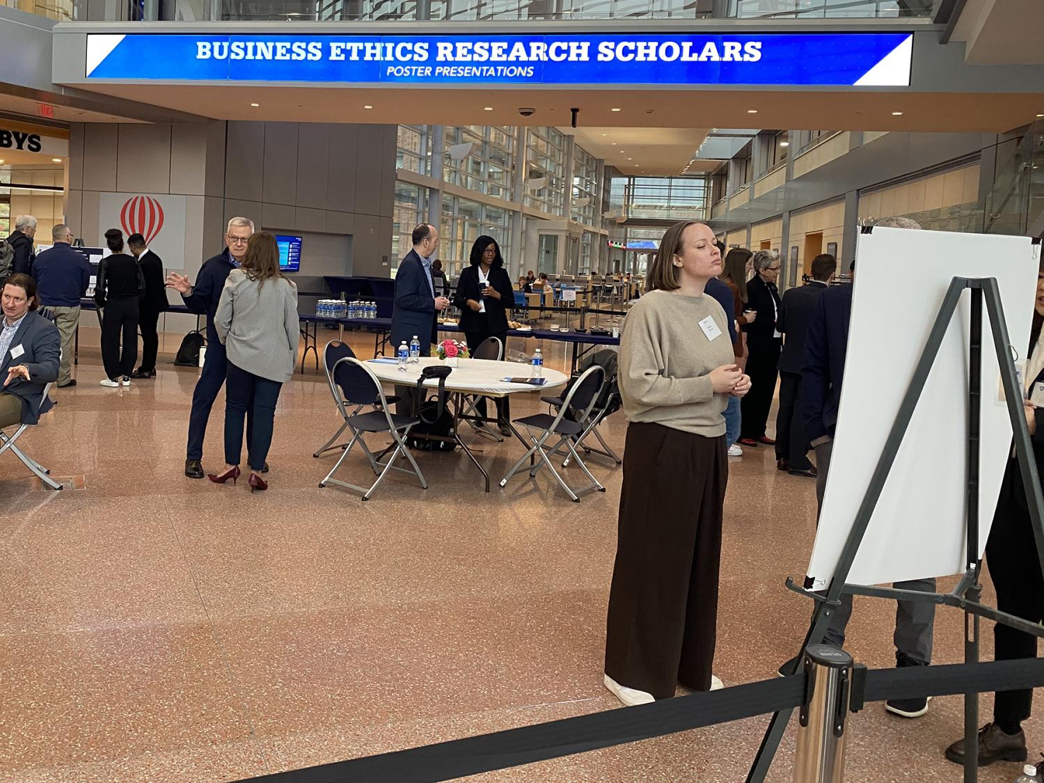 People gather in the Business Building atrium looking at poster presentations.