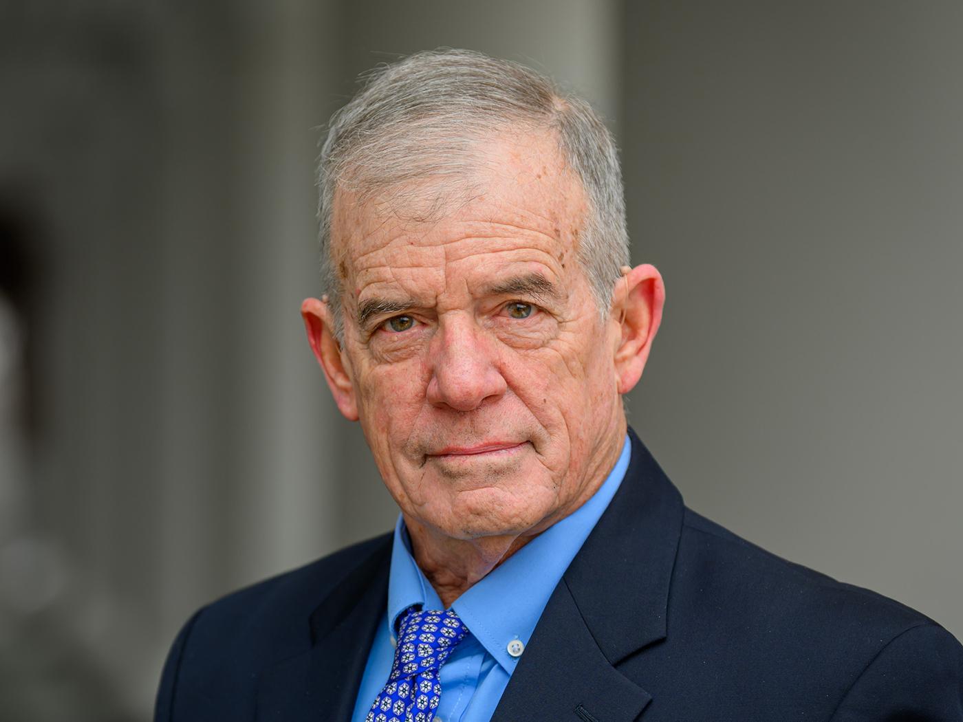 Man with short graying hair and a blue dress shirt and dark blue coat