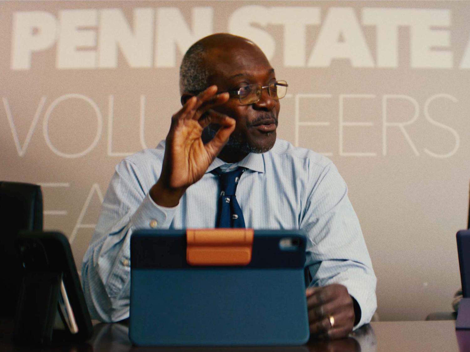 Ron Darbeau sitting at a table with a tablet device in front of him and the words Penn State Volunteers on the wall behind him.