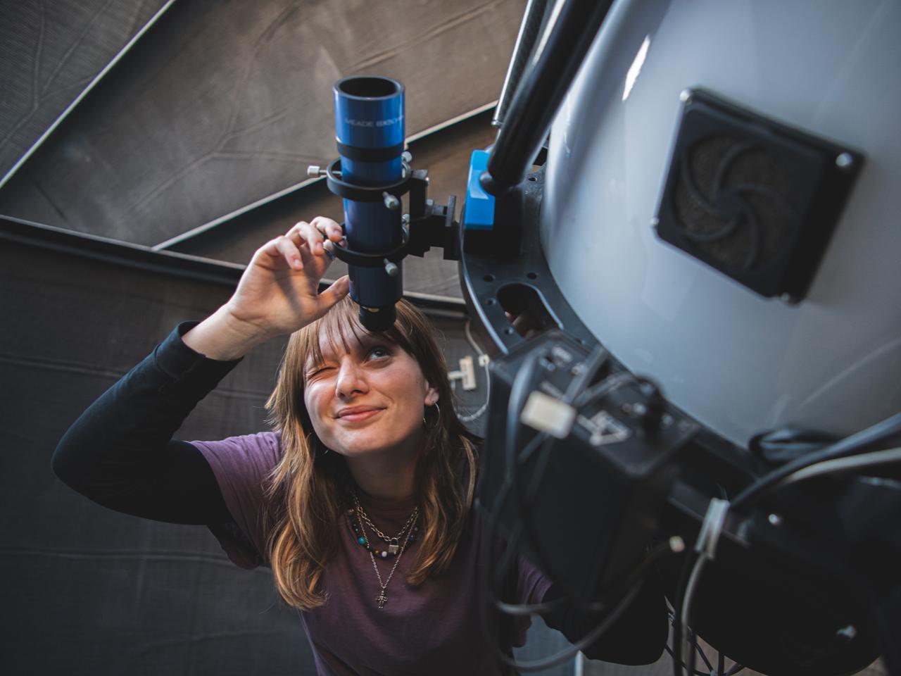 woman in purple shirt looks through telescope 