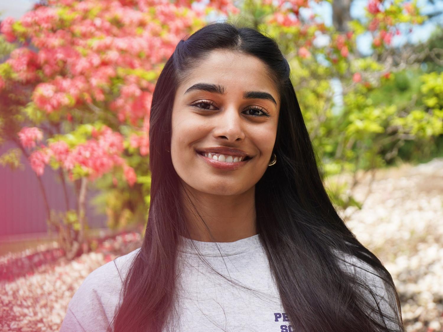Female student wearing Penn State Scranton shirt smiles with red floral trees in background.