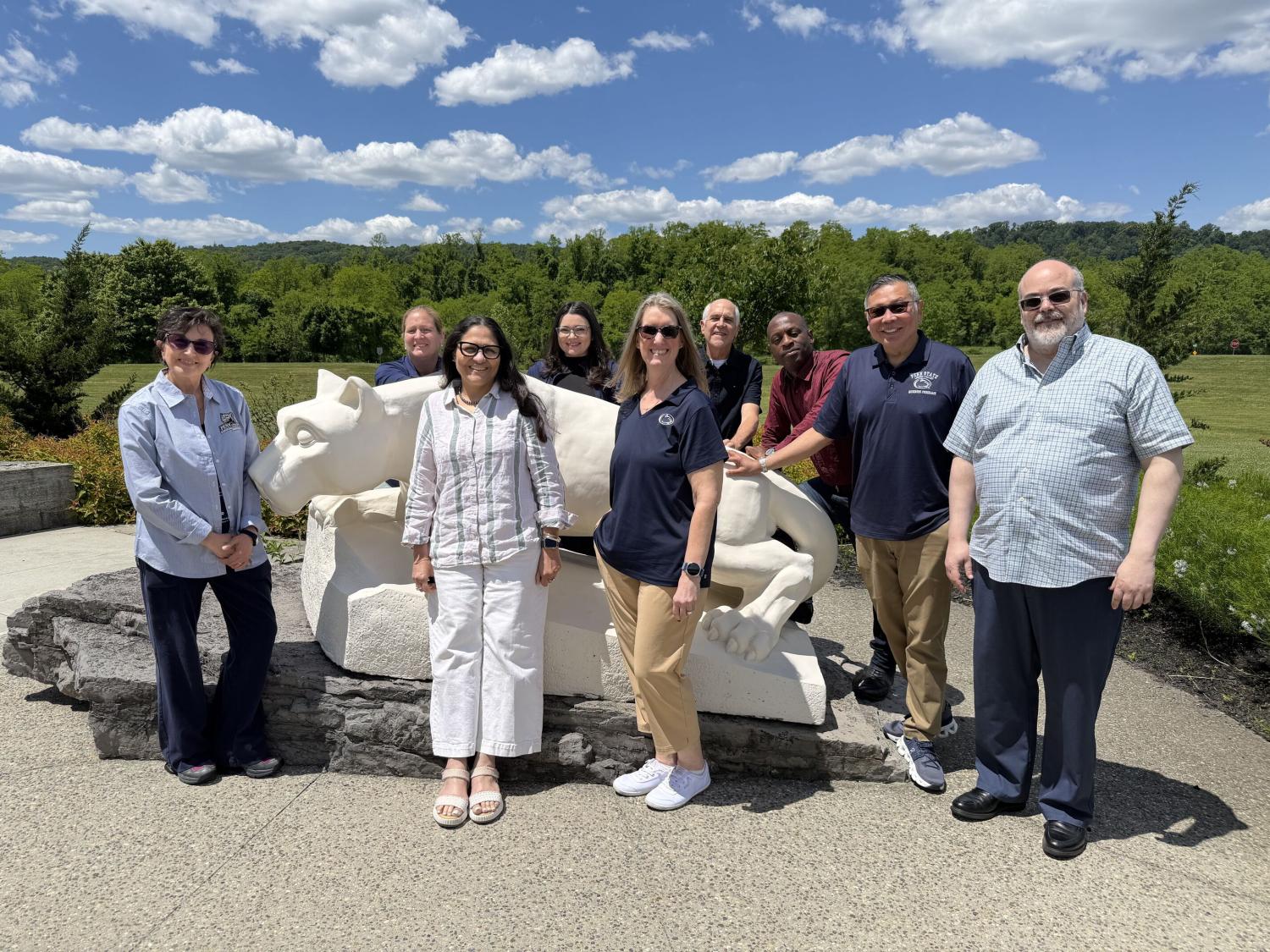 group of people standing together for a photo in front of the nittany lion statue