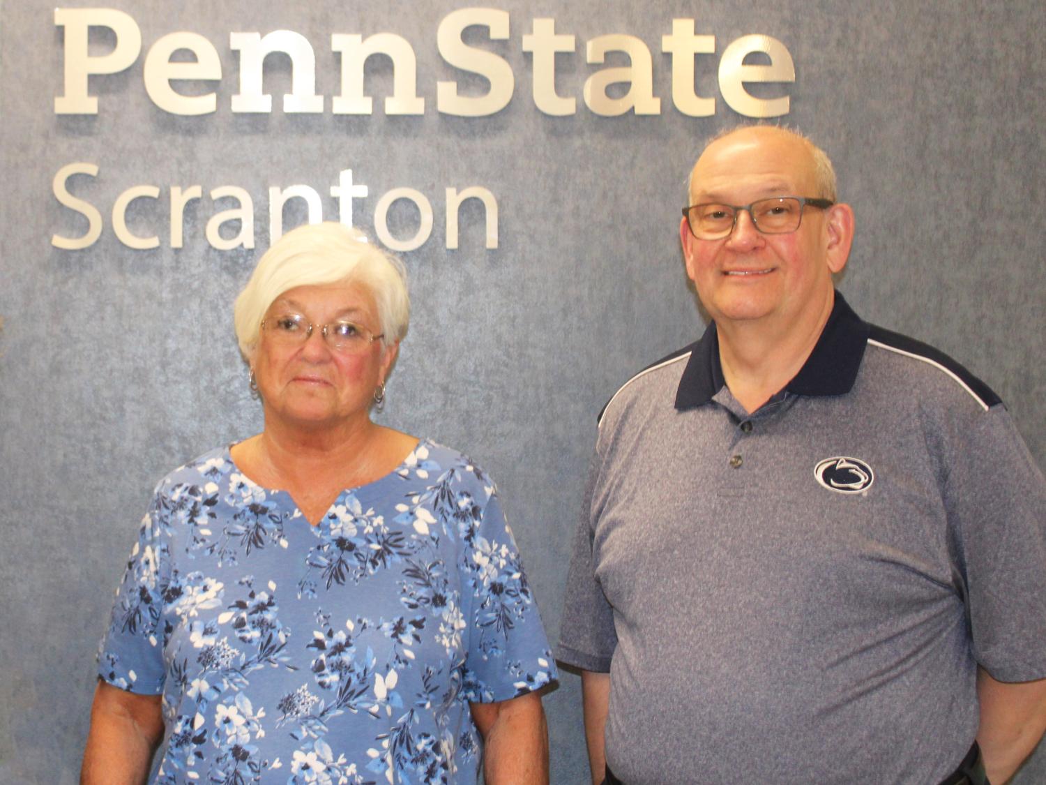 Joette Dempsey and Ed Lucy pose for a photo in front of wall with Penn State Scranton name