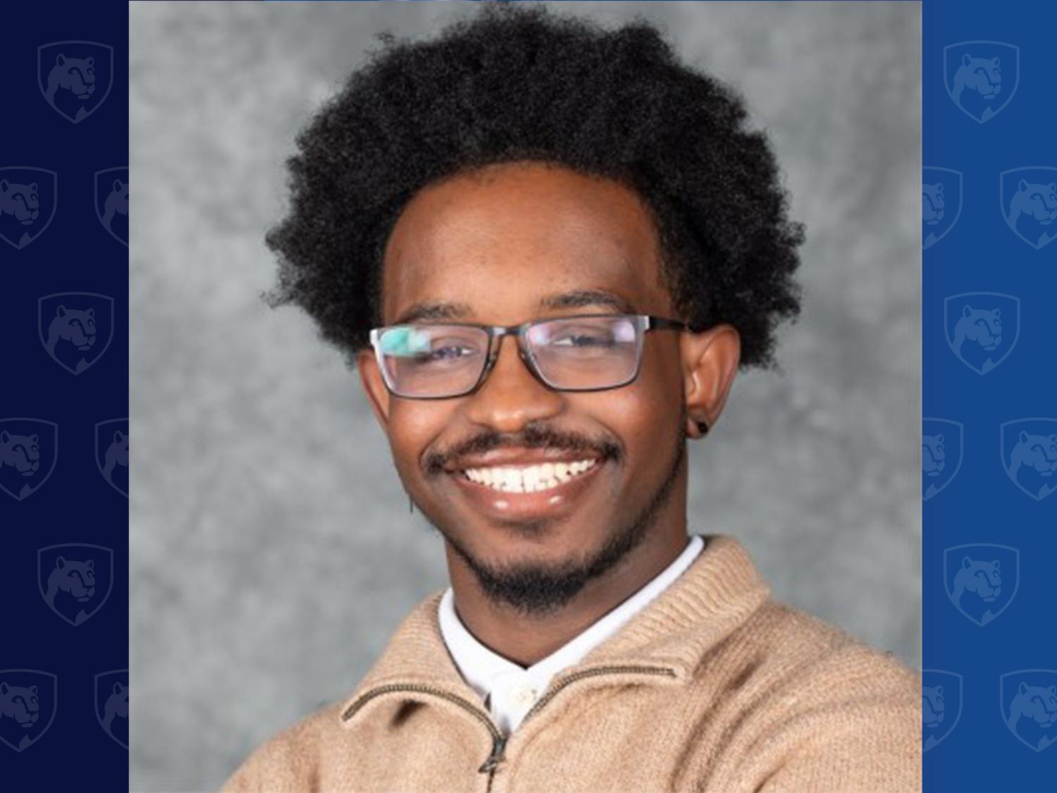 headshot of a smiling young man wearing glasses and a tan quarter zip