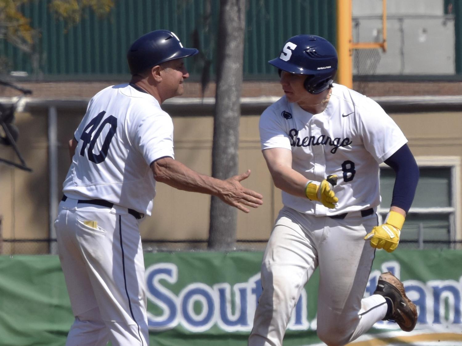 Baseball player wearing white jersey with blue helmet running and slaps the outstretched hand of a coach.