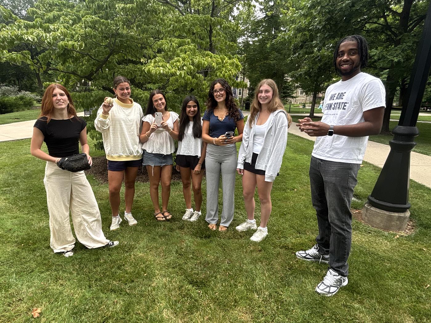 Six students standing on a grassy campus area