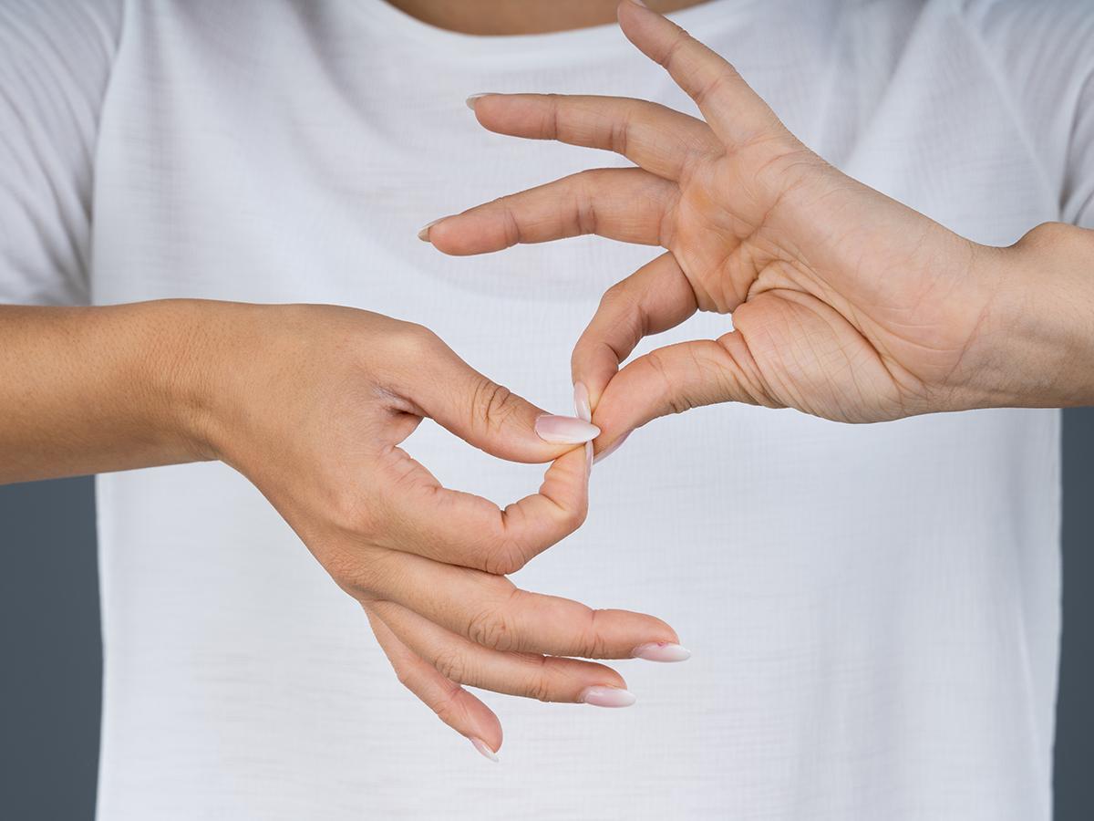 Close-up of hands forming an American Sign Language sign against a white shirt.