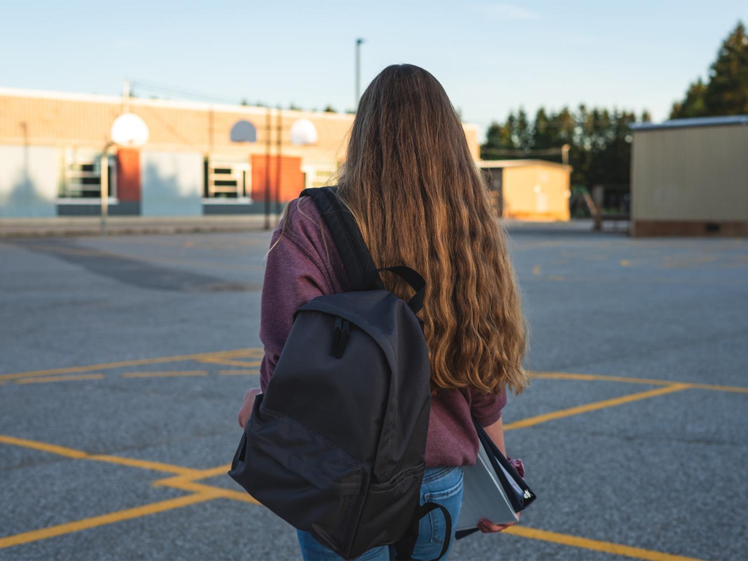 person with a backpack walks alone in a school courtyard