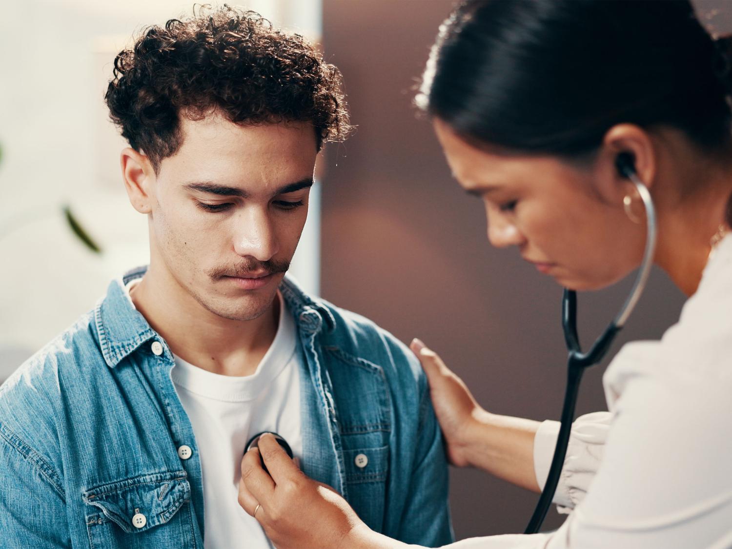 doctor checks young adult patient's heart with a stethoscope