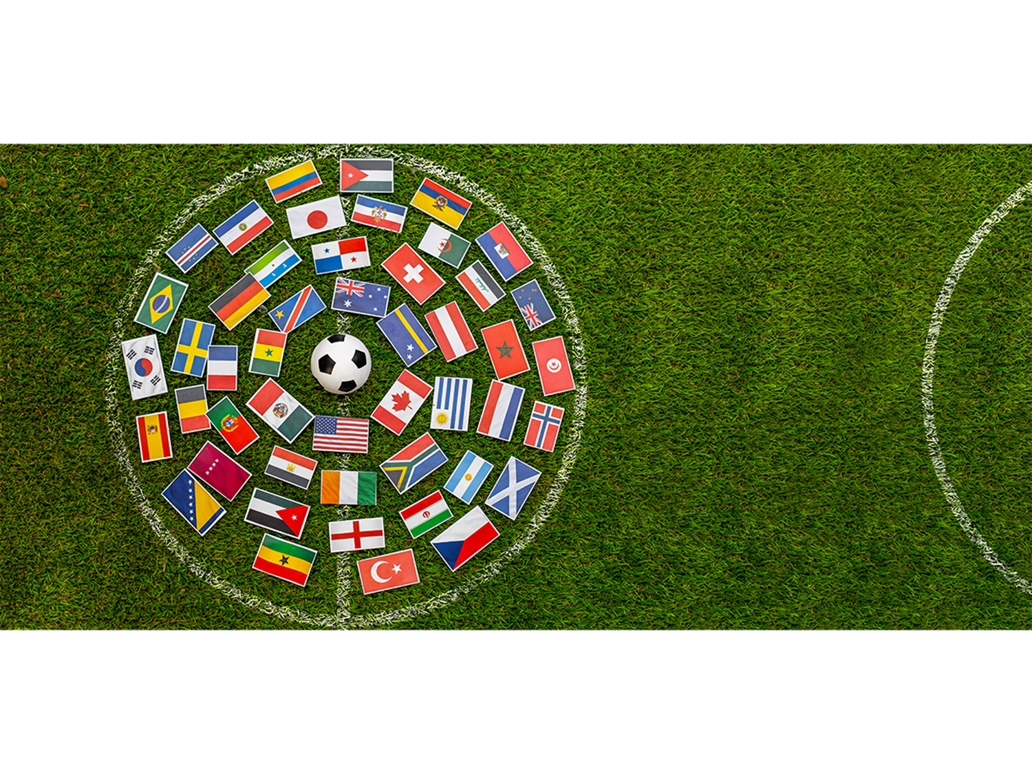 soccer ball surrounded by international flags arranged in a circle on green grass field