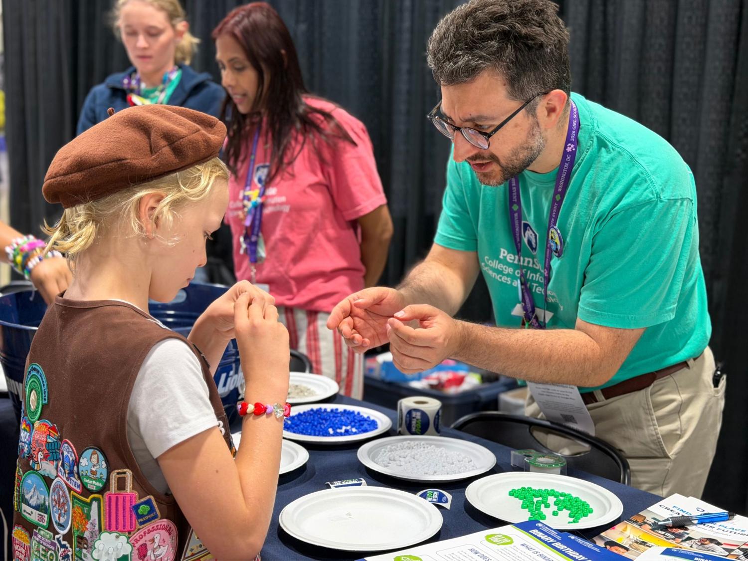 teacher helps brownie girl scout make beaded bracelet
