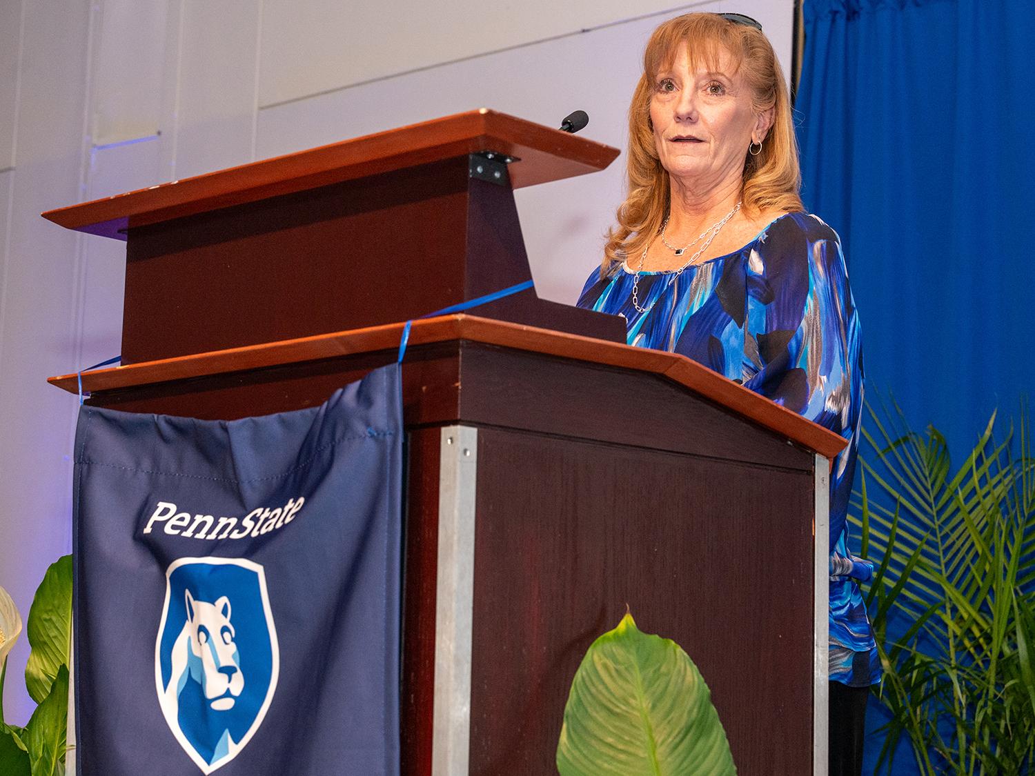 A photo of Wendy Jo Hartsock standing at a lectern with a Penn State flag on front.
