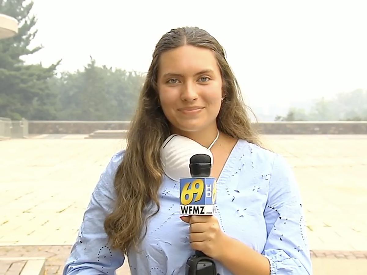 A young woman with long brown hair holding a microphone stares at the camera, 