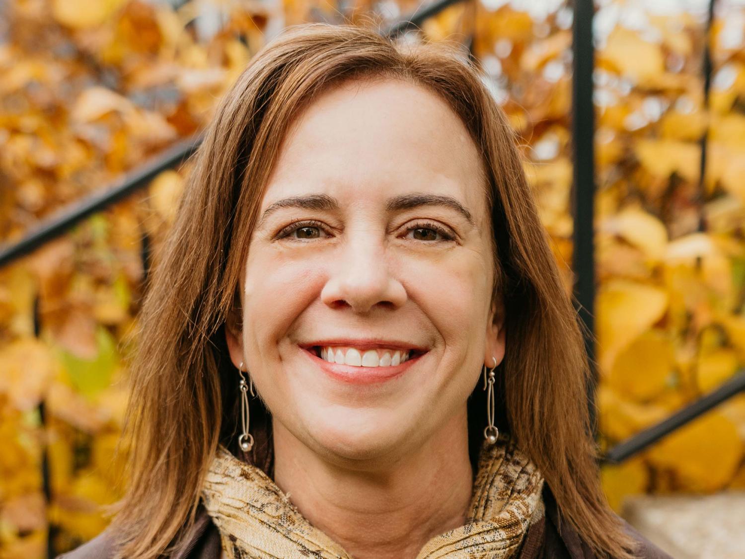 Heather Stephens, a woman with medium-brown hair smiling. Gold leaves in the background