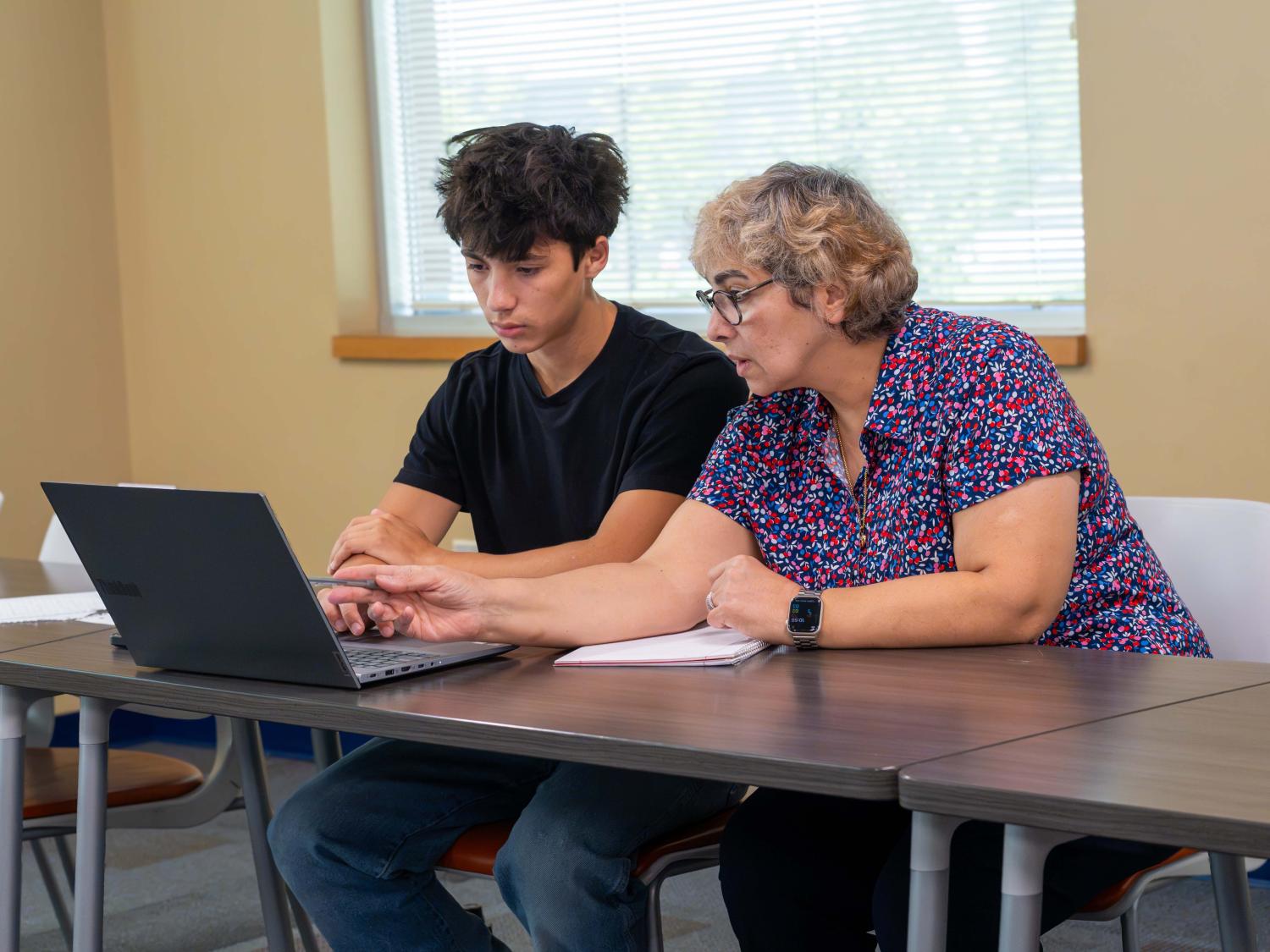 woman sitting with student and laptop at a table