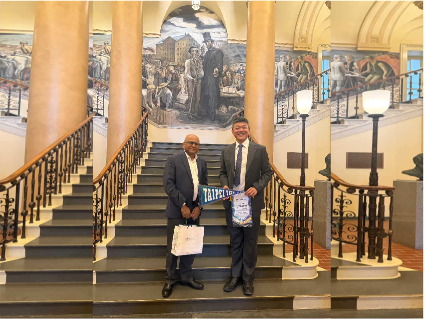 Two individuals stand on the stairs inside Old Main, smiling and holding a Taipei Tech pennant