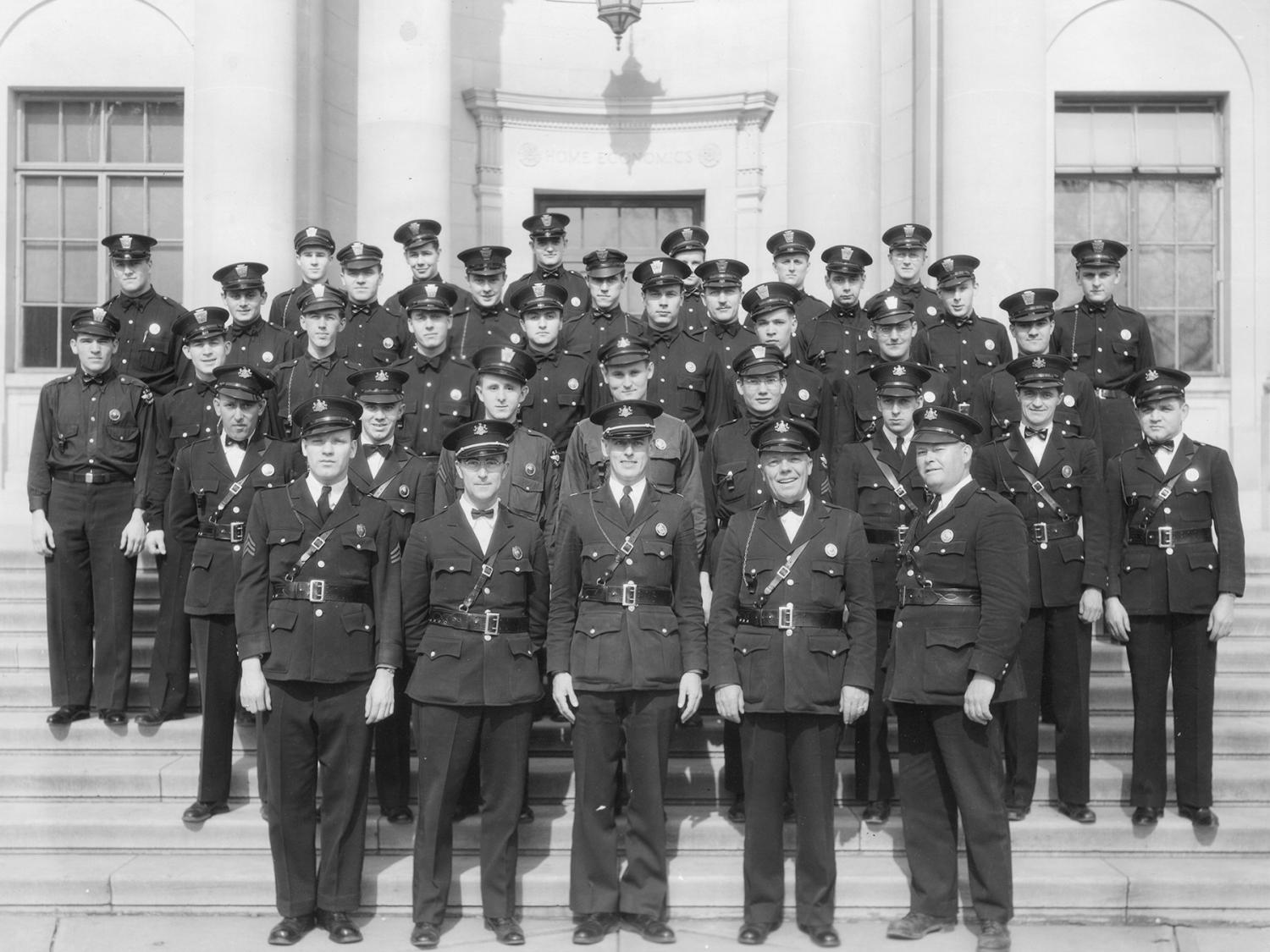 An historic photo of a group of people in uniform posing for a group photo in front of a building