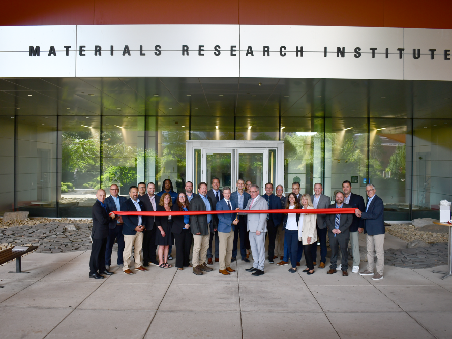 A group of people standing in front of the Materials Research Institute entrance cutting a ribbon
