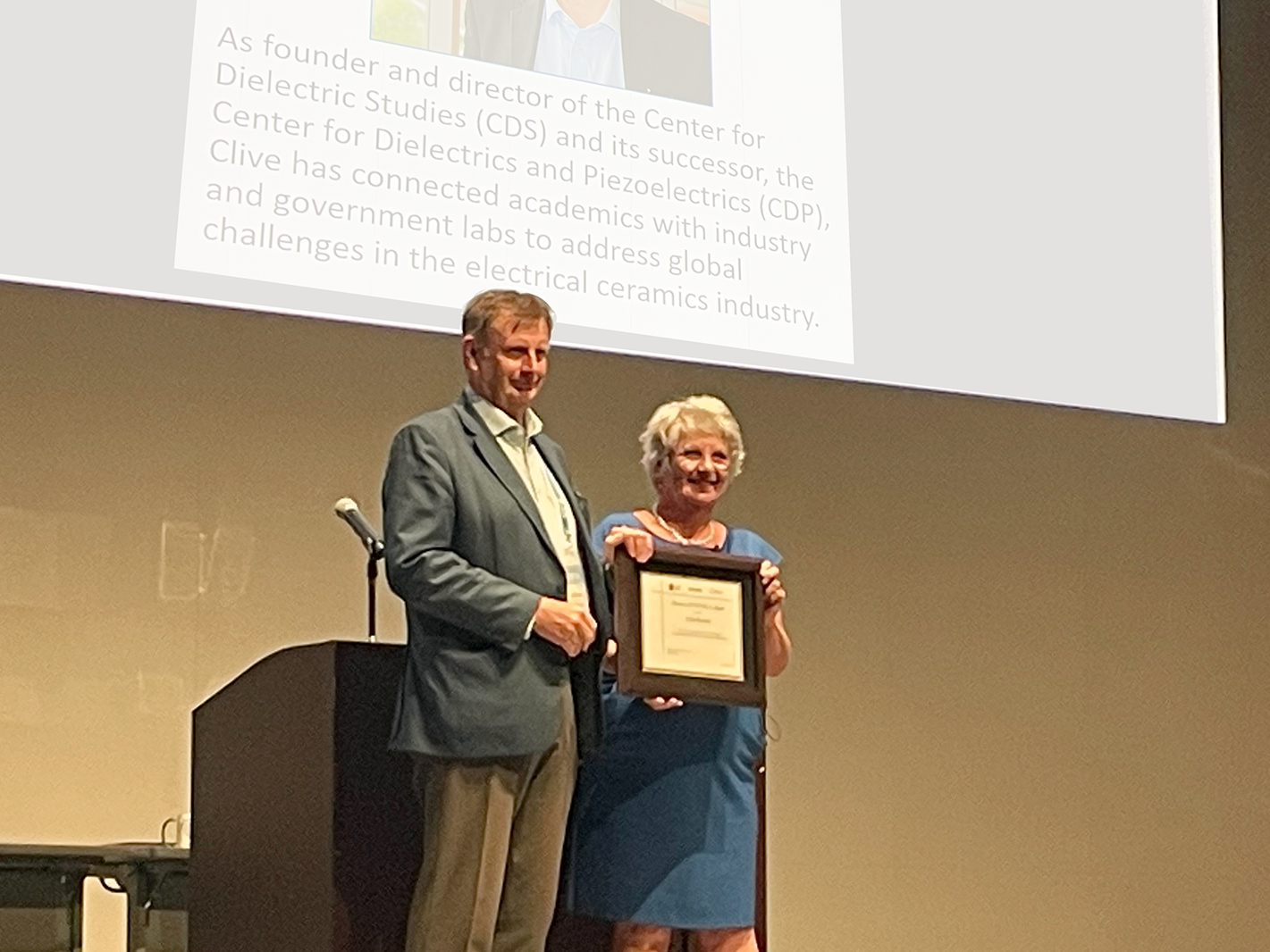 Man receiving an award from a woman on a conference stage
